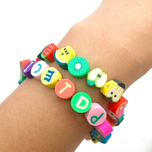 Gros plan de bracelets en perles de fruits et lettres en pâte polymère sur un poignet