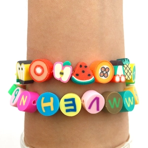 Gros plan de bracelets superposés avec tranches de fruits et perles de lettres au poignet