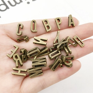 Detail of vintage bronze alloy alphabet charms held in hand for DIY jewelry making