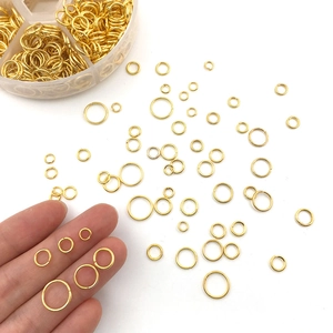 Golden open jump rings in various sizes stored in a partitioned plastic organizer box