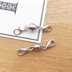 Detail of silver magnetic jewelry clasps with lobster claws on a wooden background