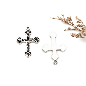Détail de pendentifs croix celtique argentée avec gravure baroque sur fond blanc