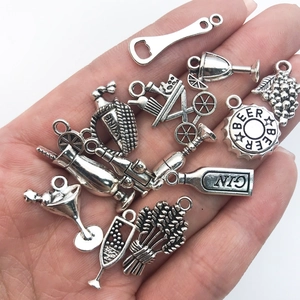 Close-up of vintage silver wine-themed charms being held in a hand for size comparison