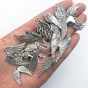 Variety of vintage silver alloy wing pendants held in hand to show actual size for DIY