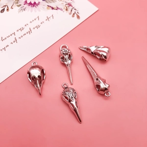Detailed set of five silver-plated gothic bird skull charms on a pink surface