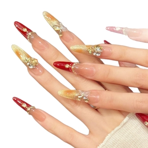 Red and gold gradient stiletto press-on nails with rhinestone accents and butterfly charms