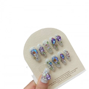Handmade purple floral press-on nails with 3D glitter crystals and pearls on white card