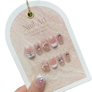 Handmade gradient pink press-on nails with 3D bows, pearls, and heart gems on a display card