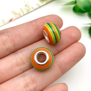 Primer plano de cuentas de resina con rayas verdes y naranjas sostenidas para ver escala
