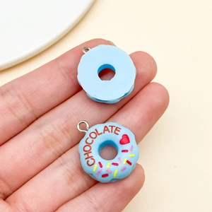 Detail of a blue resin donut charm with chocolate text and colorful sprinkles on hand