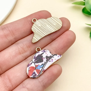 Hand holding vintage alloy hat pendants with colorful oil-drip floral pattern and gold back