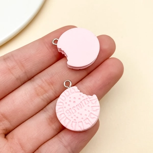 Detail of pink resin biscuit charms with BISCUITS engraving held by hand for DIY crafts