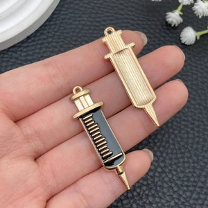 Macro view of gold alloy syringe pendants with black enamel drip detail for DIY keychains
