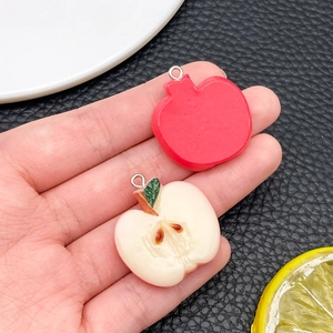 Macro detail of red apple resin charms showing whole fruit and half slice with silver loop
