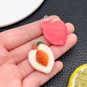 Detail shot of two resin peach charms with realistic fruit pits held in palm for scale
