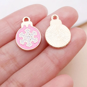 Macro shot of pink snowflake charms on fingertips showing small size for DIY jewelry
