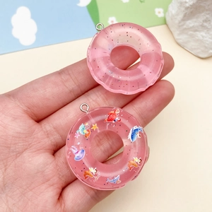 Dettaglio di ciondoli a ciambella in resina rosa con glitter e motivi marini per il fai da te