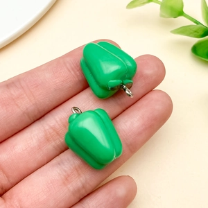 Detail von grünen Paprika Harzanhängern in der Hand, die Miniaturgröße und Glanzoberfläche zeigen