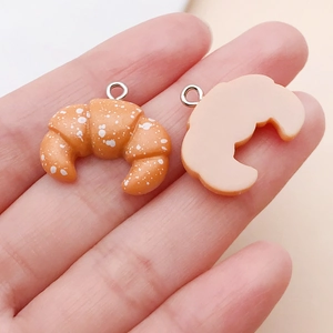Detailed close-up of a realistic resin croissant food charm held in hand for scale