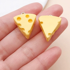 Detailed view of two miniature yellow resin cheese charms held in palm for DIY jewelry