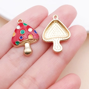 Macro view of colorful mushroom pendants on a finger showing small size and gold plating