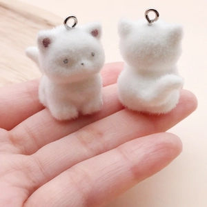 Detail of DIY white flocked kitten pendants with metal rings shown on hand for size
