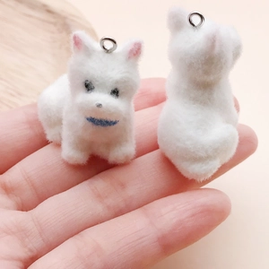 Close-up of white flocked puppy pendants held in hand for DIY jewelry and crafts