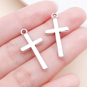 Gros plan de pendentifs croix en argent poli sur le bout des doigts montrant la taille