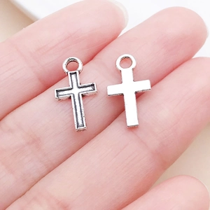 Vue macro de deux pendentifs en forme de croix argentée pour bijoux DIY tenus dans la main