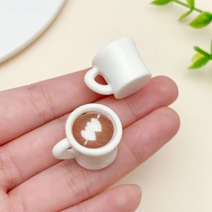 Makroaufnahme von Miniatur Kaffeetassen Anhängern mit Herz Latte Art in der Hand