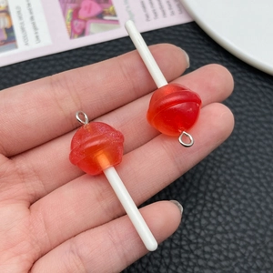 Macro detail of red glitter resin lollipop charms with silver rings held by hand
