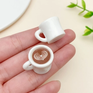 Miniatur-Kaffeetasse mit Herz-Latte-Art und winziger Becher auf Fingerspitze zur Ansicht