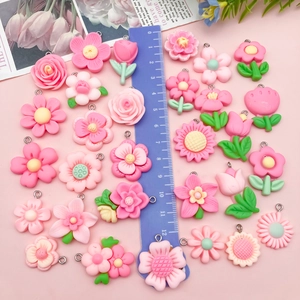Platliggende roze hars bloemen bedeltjes met metalen ogen naast een blauwe liniaal van 12 cm