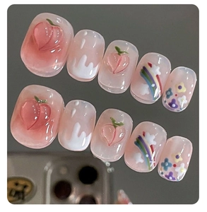 Close-up of handmade press-on nails with 3D peach charms and colorful rainbow designs