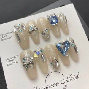 Handmade press-on nails with blue heart gems, silver bows, and pearls on nude base