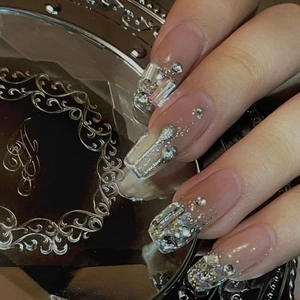 Nahaufnahme glitzernder Nude-Nagelclips mit 3D-Silber-Strasssteinen auf Metalltablett