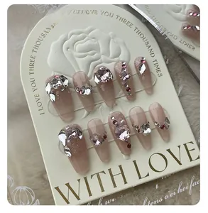 Macro detail of nude pink handmade press-on nails with crystal hearts and rhinestones