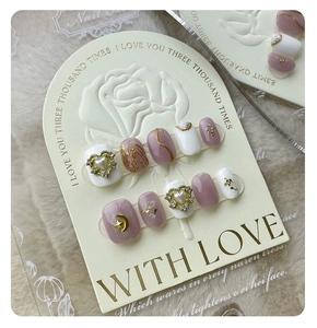Macro detail of handmade press-on nails with pink base, 3D pearl heart, and gold foil accents