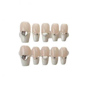 Set unghie finte crema con perle, strass e decorazioni a cuore su sfondo bianco pulito