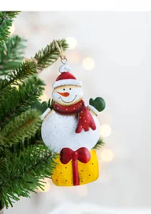 Detail of metal snowman ornament with festive red scarf hanging on a Christmas tree branch