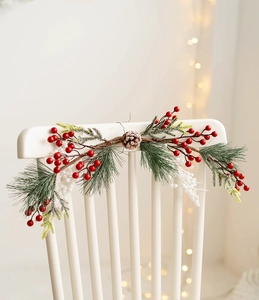 Close-up of Christmas wreath with red berries, pine needles, and pine cones on white wood