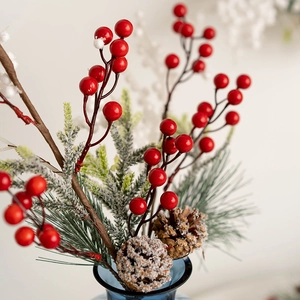 Christmas wreath branch with red berries and pine cones in a blue glass vase