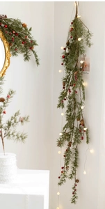 Close-up of Christmas pine garland with red berries, pinecones and warm LED ball lights