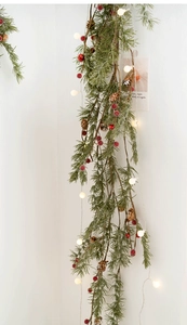 Close-up of pine branches with red berries, pine cones and warm LED string lights