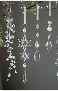 Macro detail of acrylic snowflake and teardrop pendant on a Christmas tree branch