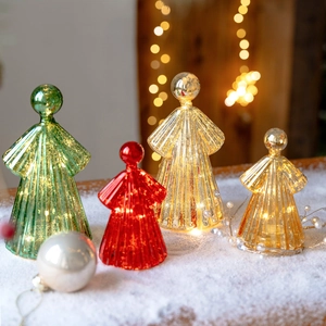 Lighted glass angel Christmas ornaments with warm LED lights on white snowy surface