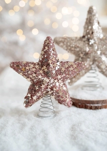 Detail of rose gold glitter star tree topper with a spring base on snowy background
