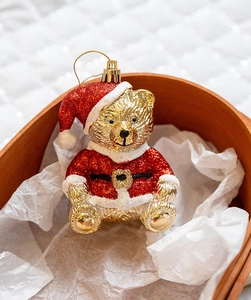 Close-up of golden Christmas bear ornament with red glitter suit on wooden tray