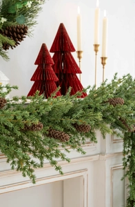 Christmas pine needle garland with brown cones on white fireplace with paper trees