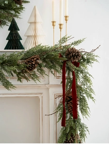 Close-up of Christmas PE garland with pine cones and red velvet ribbon on a white mantel